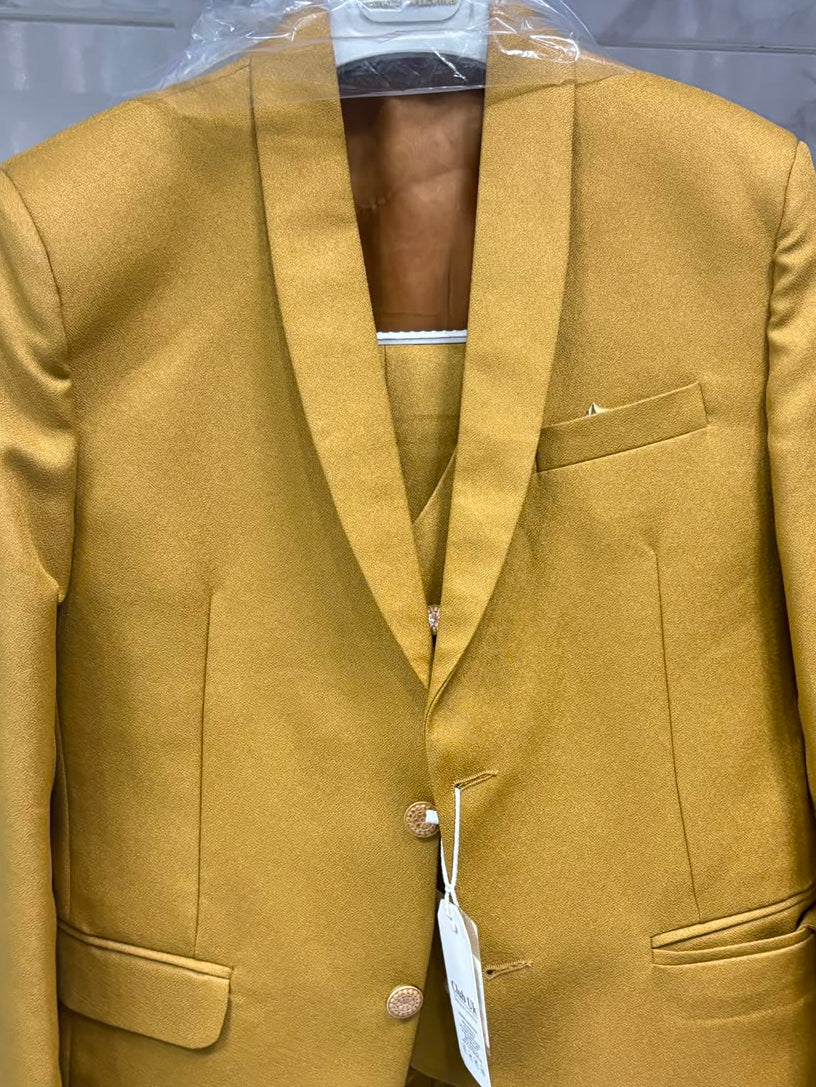 A mustard yellow tailored blazer jacket with a matching vest and trousers set, hanging on a hanger wrapped in protective plastic against a gray tiled wall.