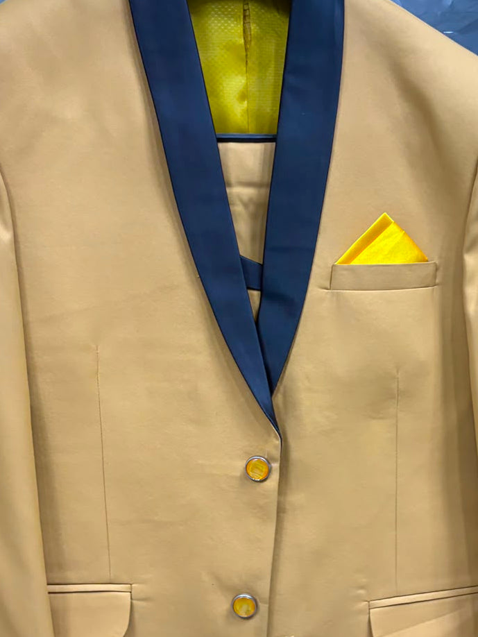 A men's formal blazer in tan with dark navy shawl lapels, featuring a matching yellow pocket square and yellow inner lining, displayed on a hanger.