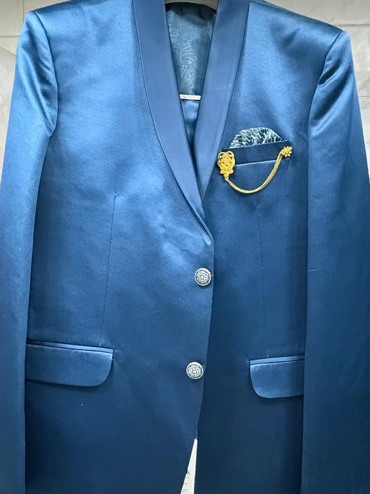 A blue satin blazer jacket with notched lapels, two silver buttons, flap pockets, and a decorative gold and blue pocket square, hanging on a rack.