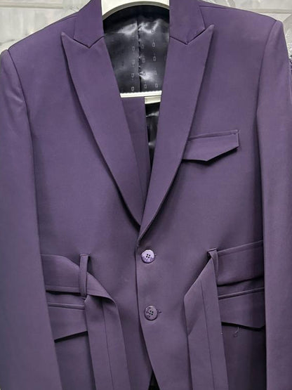 A purple tailored blazer jacket hanging on a hanger, with matching tie details at the waist, photographed in a retail or storage setting with other garments partially visible.