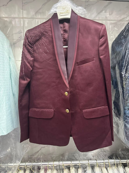 A men's maroon velvet blazer jacket with gold buttons and gold trim on the collar, hanging on a hanger in a retail setting.